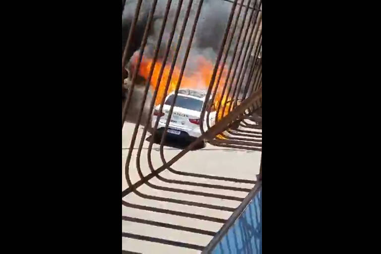 imagem de carro branco em chamas ao fundo com grade na frente