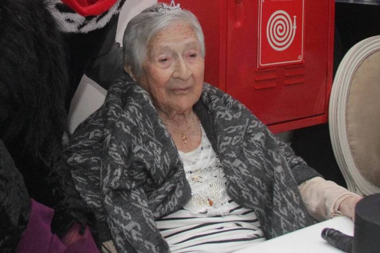 Senhora idosa sentada em cadeira, tem expressão serena, é branca e tem cabelos curtos brancos