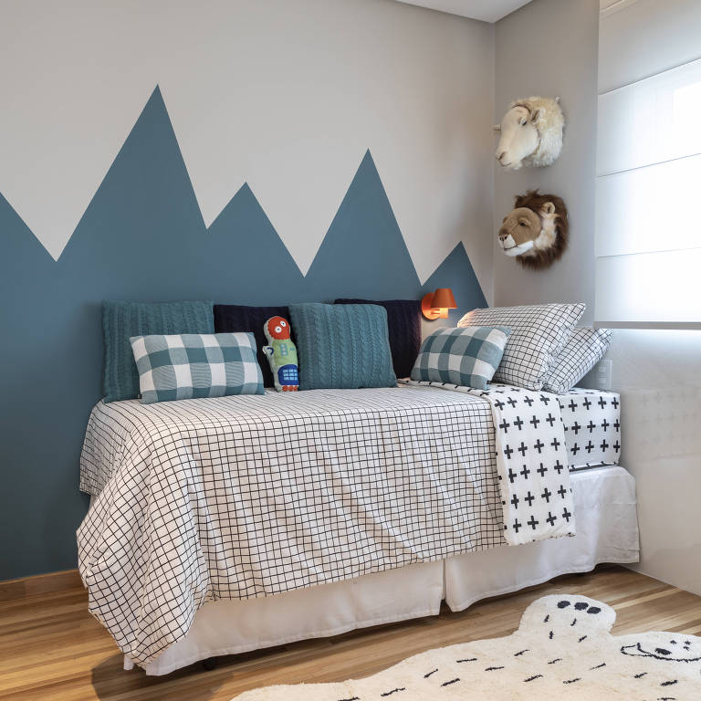 Quarto infantil com parede pintada em formato geométrico no formato de montanhas, a cor é azul acinzentado. O quarto tem uma cama de solteiro e enfeites com a temática de animais