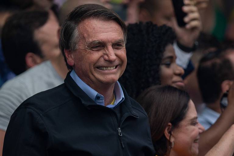 O presidente Jair Bolsonaro, durante campanha para reeleição na praça do Pacificador, no centro de Duque de Caxias, na Baixada Fluminense. É um homem branco, que veste uma jaqueta preta. A imagem o mostra sorrindo

