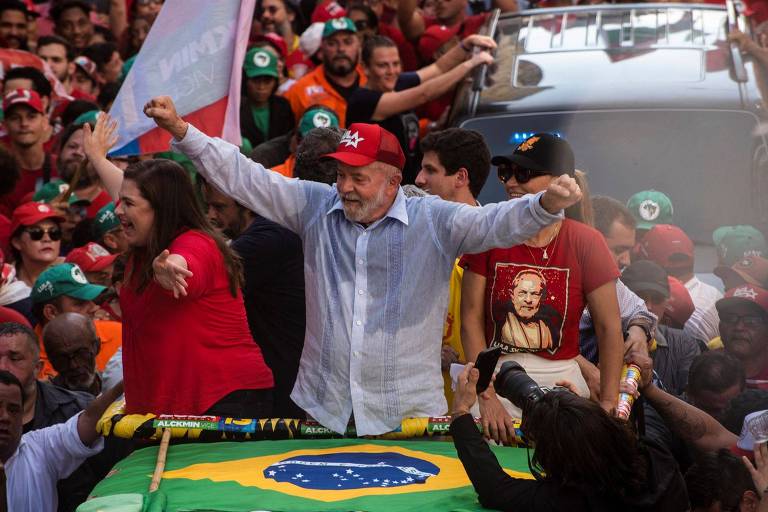 De braços abertos, usando um boné vermelho e em um carro aberto, o ex-presidente Lula em evento no Recife