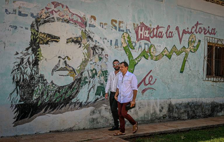 Lazaro Gonzalez, 52, e Adiel Gonzalez, 32, caminham em frente a muro com imagem de Che Guevara após se casarem em Bolondron, em Cuba
