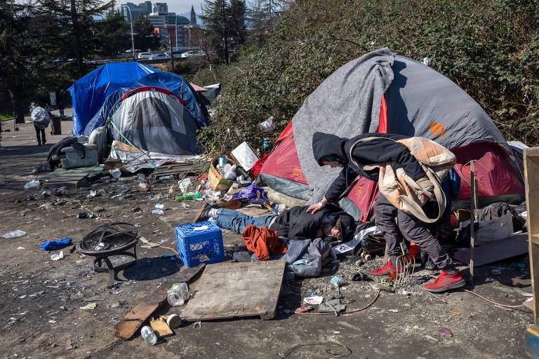 Homem em situação de rua verifica condição de um amigo que desmaiou depois de fumar fentanil em um acampamento em Seattle, nos EUA