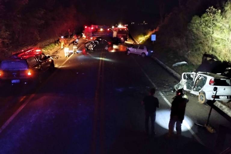 A foto mostra uma estrada à noite com carros acidentados