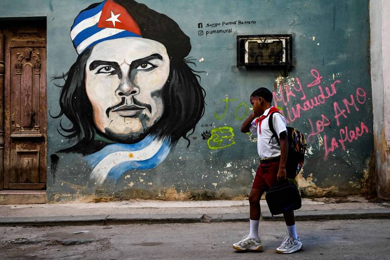 Um estudante caminha pelas ruas de Havana, com uma imagem de Che Guevara ao fundo