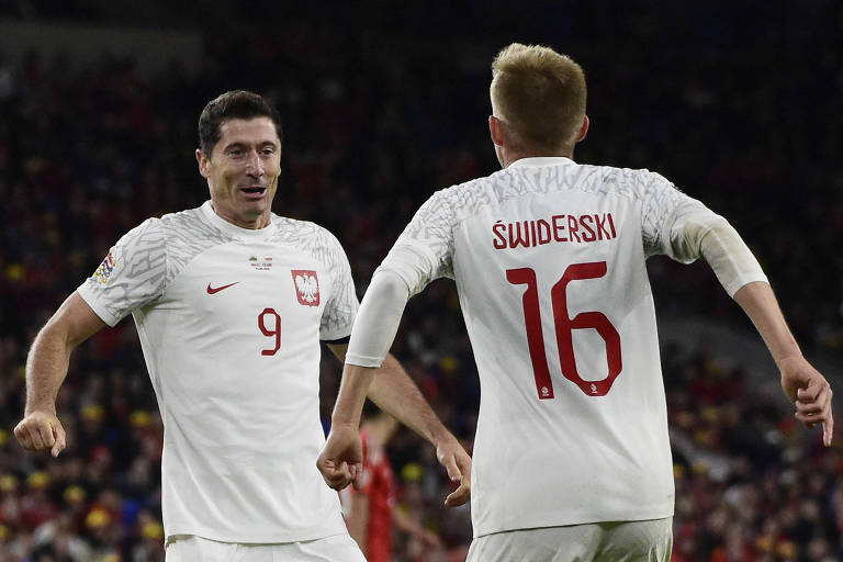 De uniforme branco e com o número 9 em vermelho na altura do peito, Lewandowski celebra diante do compatriota Swiderski, que está de costas e usa o número 16, gol da Polônia diante do País de Gales, pela Liga das Nações, em Cardiff