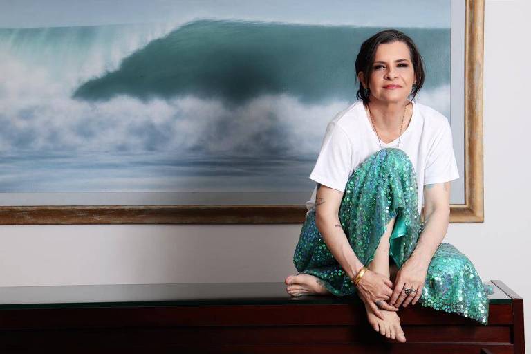 Marina lima sentada em um móvel escuro, de costas para um quadro em que se observa uma onda quebrando