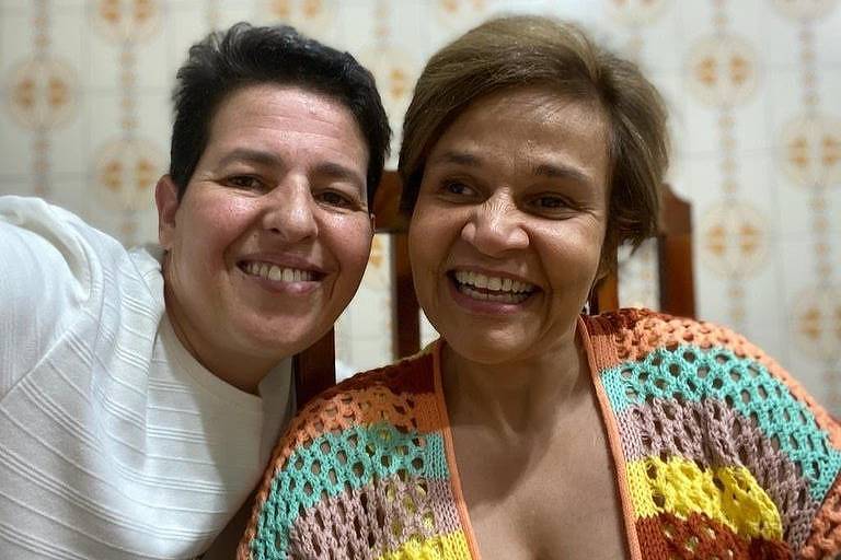 Em foto colorida, duas mulheres sorriem ao posarem juntas para uma foto