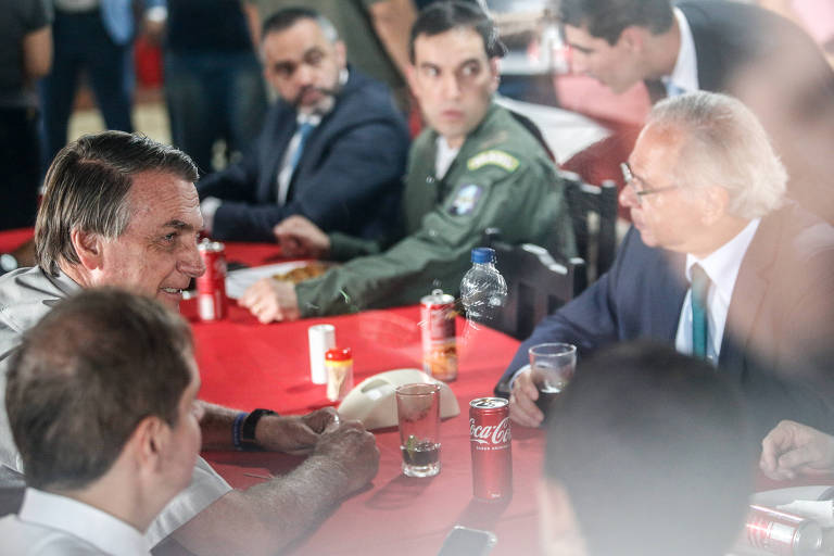 Imagem mostra o presidente Jair Bolsonaro em uma mesa de restaurante, acompanhado de diversos assessores, entre eles o ministro da Economia, Paulo Guedes. Eles conversam.