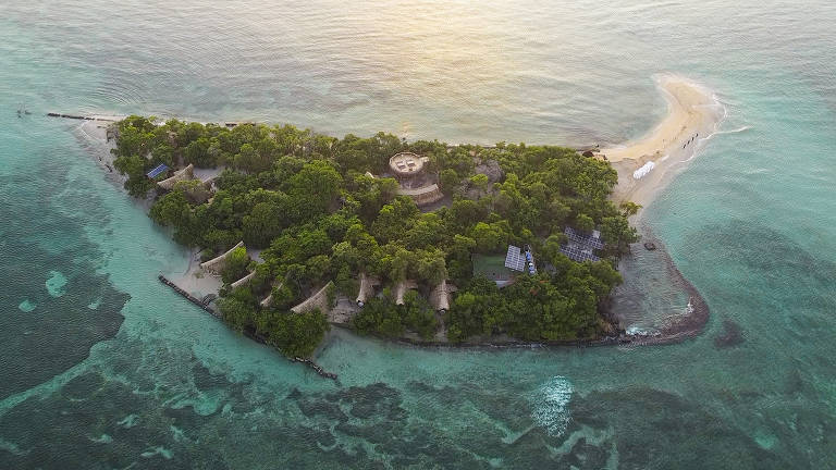 Fotografia colorida com vista aérea da ilha Corona, com árvores e mar