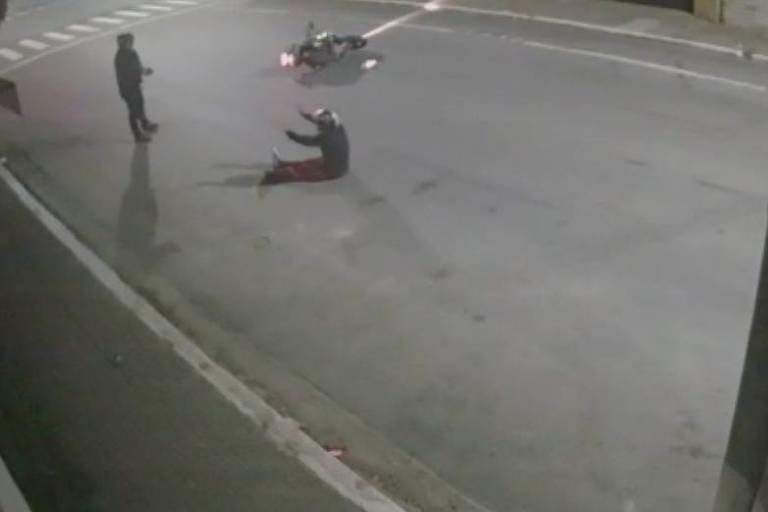 Imagem mostra vítima de tentativa de assalto em pé, segurando arma, enquanto ladrão baleado está sentando no chão