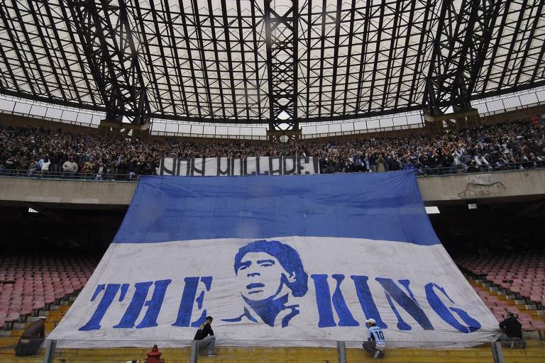 Bandeira gigante com os dizeres "O Rei" e a imagem do rosto de Diego Maradona é estendida por torcedores no estádio do Napoli, na Itália