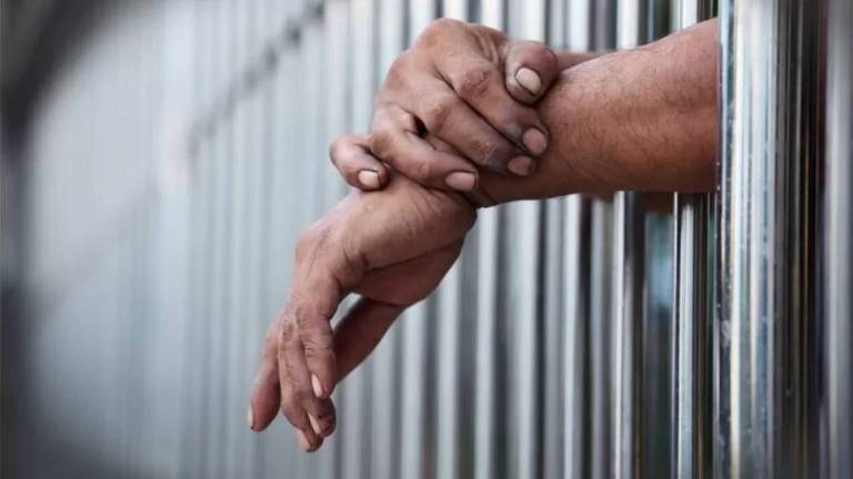 Prisioneiro passa as mãos por entre as grades de sua cela