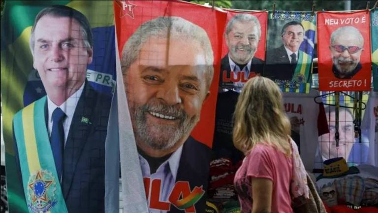 Mulher passa por muro onde estão estendidas toalhas com os rostos dos candidatos Lula e Bolsonaro