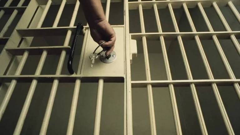 Mão de carcereiro coloca a chave dentro de uma fechadura de cela