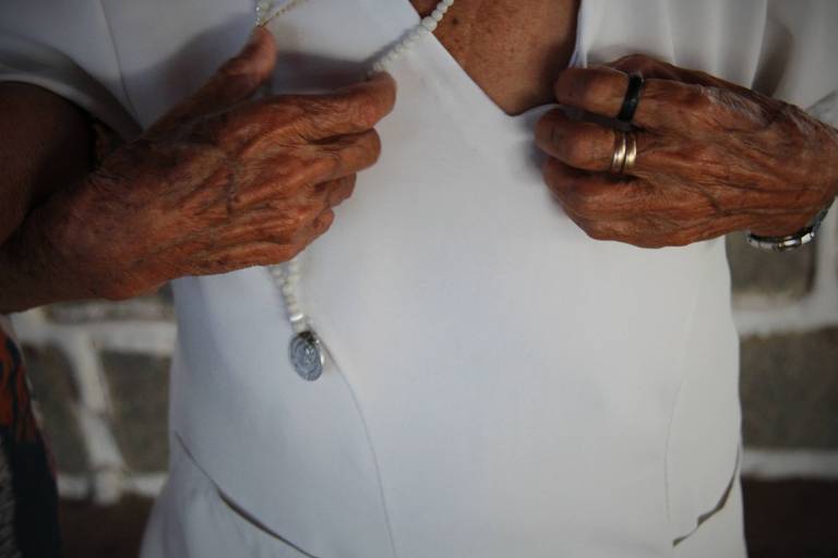 detalhe de terço branco em mãos de idosa que veste branco