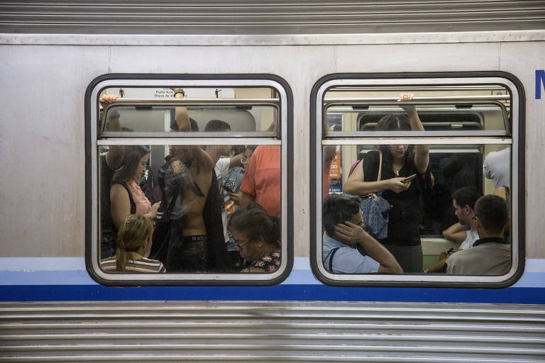 Retrato mostra duas janelas do vagão do metrô, que está lotado de passageiros internamente