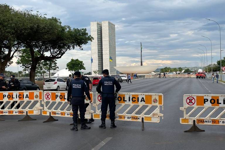 barricada em frente à praça dos três poders, com o congresso oa fundo e dois policiais na frente