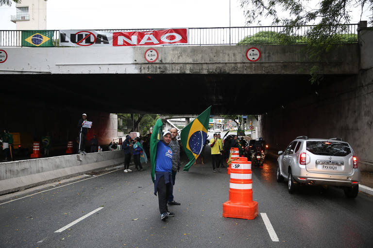 Manifestantes seguram bandeiras do Brasil sob ponte; acima, faixa com as palavras "Lula Não"