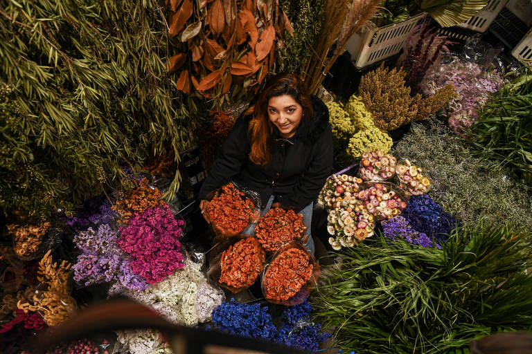 A vendedora Beatriz Silva entre as folhas e plantas no estande em que trabalha no Mercadão das Flores, perto do Ceagesp