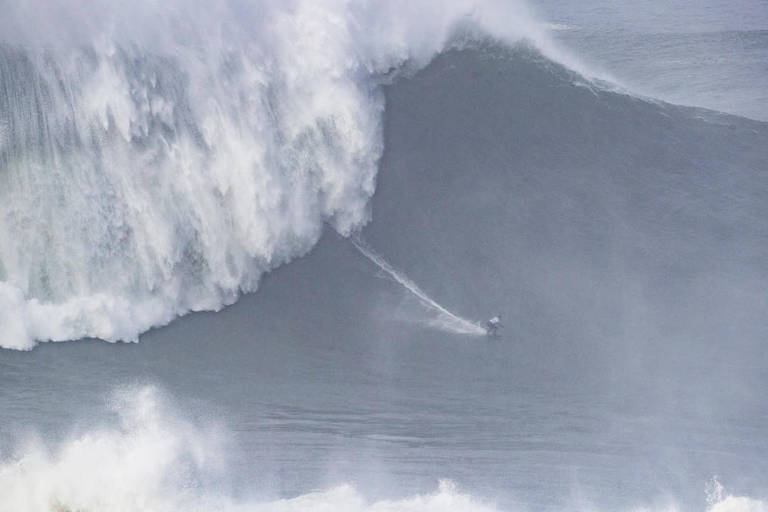 A surfista Maya Gabeira surfando em pé em sua prancha em uma onda gigante