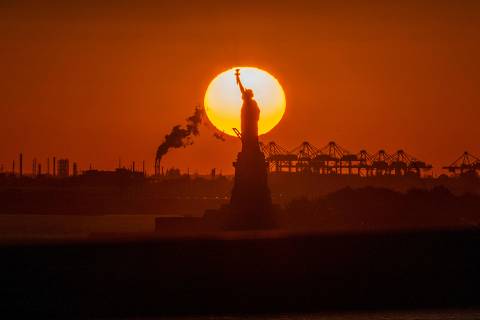 TOPSHOT - The sun sets behind the Statue of Liberty in New York on November 3, 2022. (Photo by ANGELA WEISS / AFP)