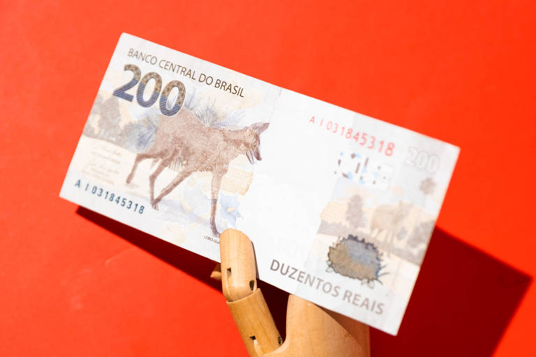 Imagem mostra mão de madeira segurando nota de R$ 200,00.