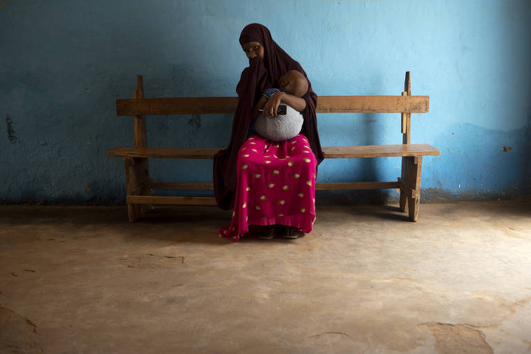 Mãe segura filho desnutrido no colo enquanto aguarda atendimento em clínica de Baidoa, na Somália