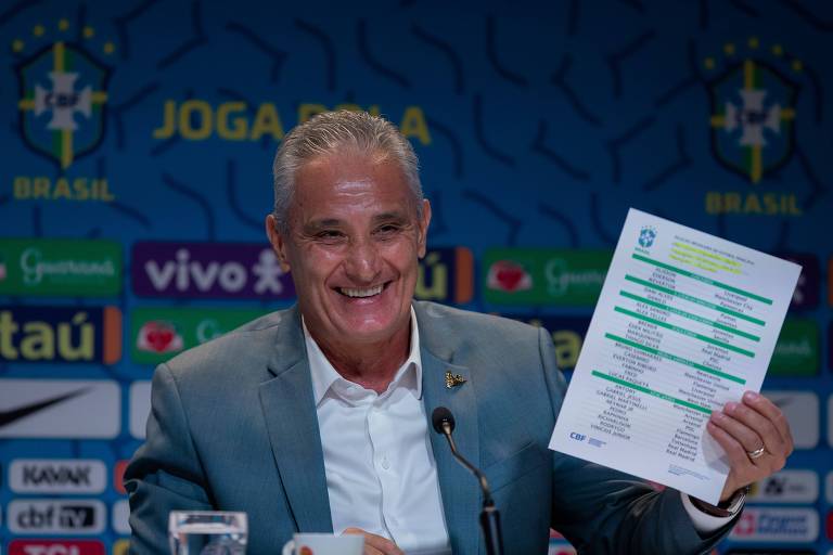 O técnico da seleção brasileira Tite, de terno cinza, segura a lista com o nome dos convocados para a Copa do Mundo do Qatar