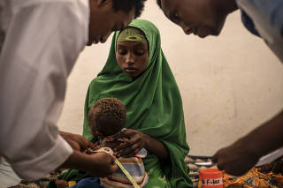 Udugow Mohamed holds her 10-month-old-son, Yazeed Osman, while the thickness of his upper arm was measured by doctors in Baidoa, Somalia, on Nov. 3, 2022. (Andrea Bruce/The New York Times)