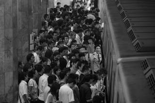 A subway staffer speaks to keep order as passengers crowd into a train in Beijing