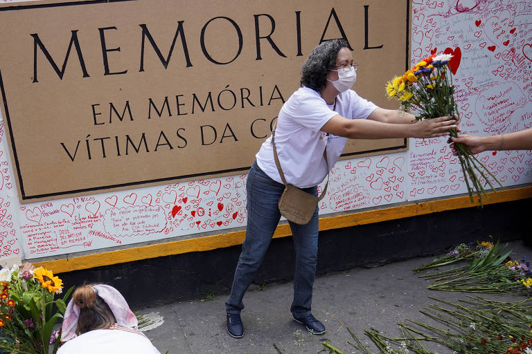 Mulher coloca flores no memorial criado na avenida Paulista, em São Paulo, em homenagem às vítimas da Covid-19