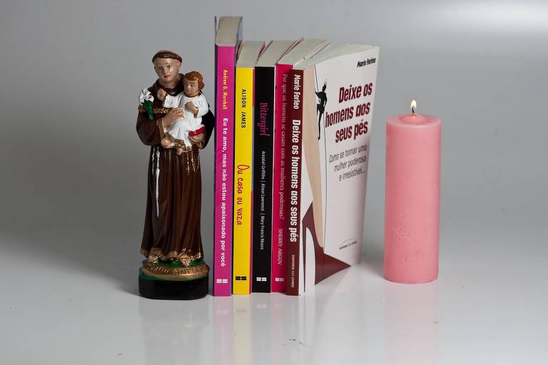 Imagem de Santo Antonio, ladeada por cinco livros em pé e uma vela cor de rosa