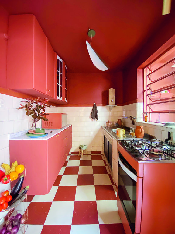 Cozinha com bancada, parede, teto, armário e eletrodomésticos todos no mesmo tom de rosa. O chão é quadriculado de rosa e branco