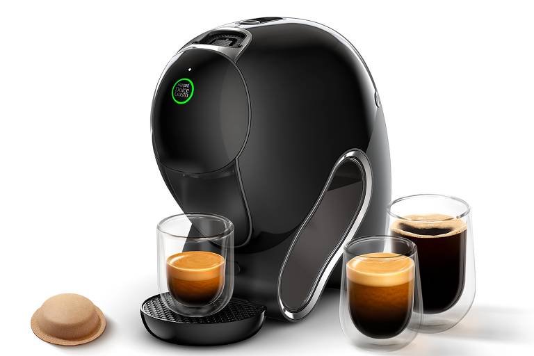Máquina de café da cor preta, com xícaras de café no entorno e cápsula de café em papel