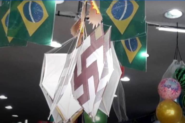 A imagem colorida mostra bandeiras do Brasil e pipas com desenhos que parecem uma suástica