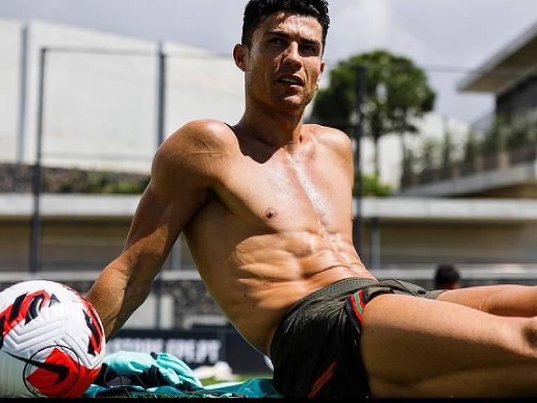 Cristiano Ronaldo, jogador da seleção de futebol de Portugal, sentado sem camisa ao lado de uma bola de futebol