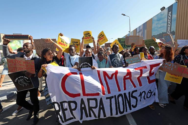 Grupo caminha com faixa "climate reparations" (reparações climáticas)