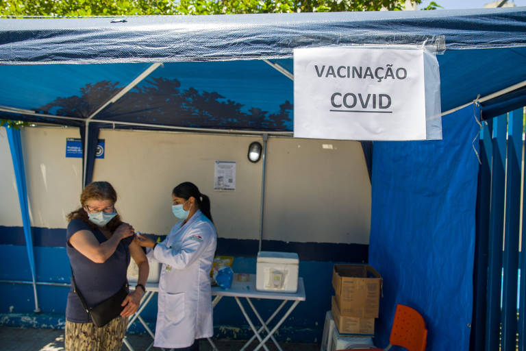 Mulher com avental branco e máscara aplica vacina contra Covid 
