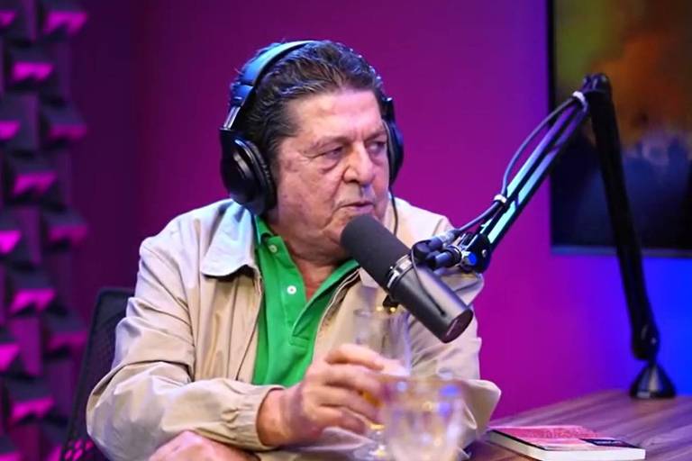 Em foto colorida, homem de camisa verde e casaco creme dá entrevista em estúdio