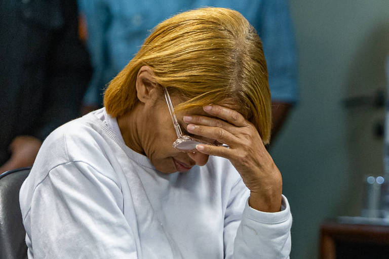 Foto da ex-deputada Flordelis no tribunal, durante julgamento; ela está sentada e com a cabeça baixa, apoiada com uma das mãos, vestindo blusa de moletom branca e calça jeans azul