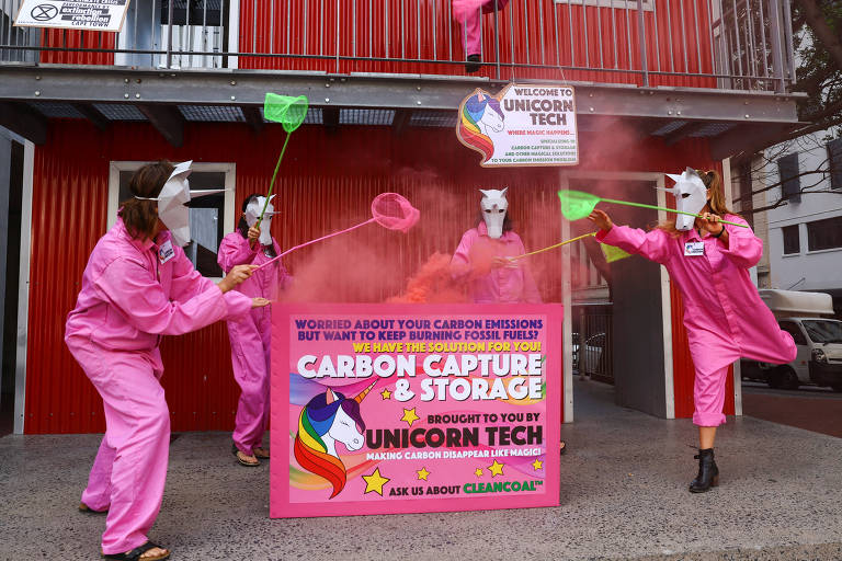 Pessoas vestidas com macacões rosa e cabeças de unicórnio "capturam" um pó cor de rosa lançado ao ar com redes de caçar borboleta. Entre eles há um cartaz que imita uma propaganda de um serviço oferecido por unicórnios para ações mágicas contra emissões de carbono, em ironia