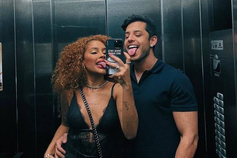 Em foto colorida, casal se diverte ao fazer selfie em elevador