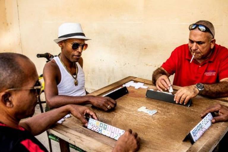 Imagem mostra homens em uma mesa jogando dominó