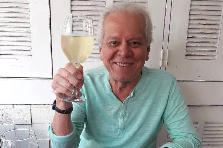 Ricardo Gontijo é um homem branco de 78 anos. Ele usa uma camiseta de manga longa em tom verde claro e segura uma taça de champagne. 