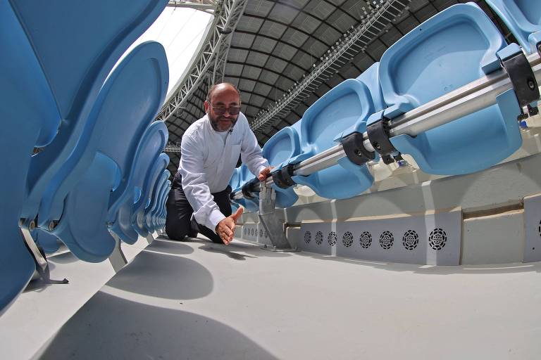 Saud Abdul Ghani mostra como funciona no setor dos torcedores a tecnologia de refrigeração no estádio Al Janoub, que receberá jogos da Copa do Mundo; o sistema de ventilação opera sob as cadeiras azuis nas quais o fã se sentarão