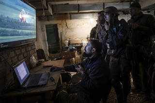 A drone operator shares footage of an attack against a Russian position with fellow soldiers of the Ukrainian army?s Carpathian Sich Battalion at an underground base in the Kharkiv region of Ukraine, May 11, 2022. (Lynsey Addario/The New York Times)