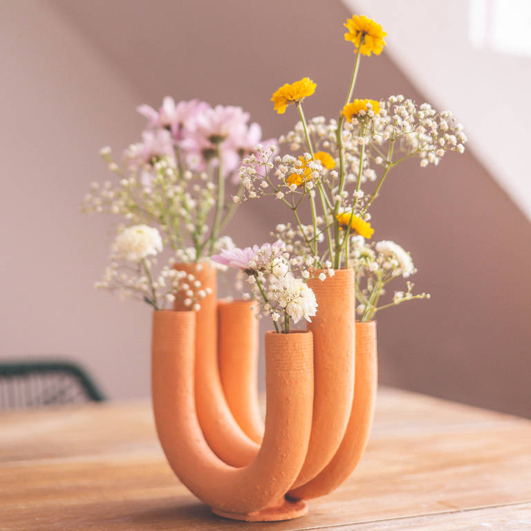 Vaso de flores com tubos curvos laranjas em cima de uma mesa de madeira
