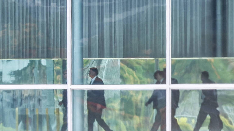 fotografia colorida é retrato tirado de longe de Bolsonaro, visto caminhando dentro do Palácio do Alvorada, cujas paredes são de vidro 
