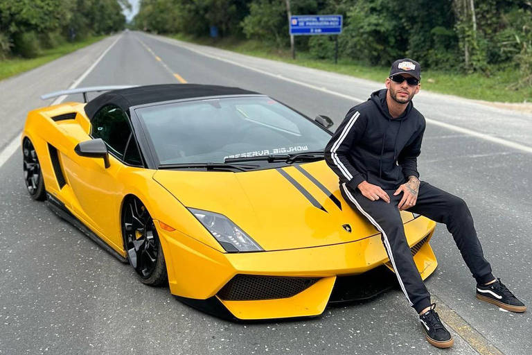O influenciador aparece sentado em um carro amarelo, da marca Lamborghini, que está no meio de uma estrada